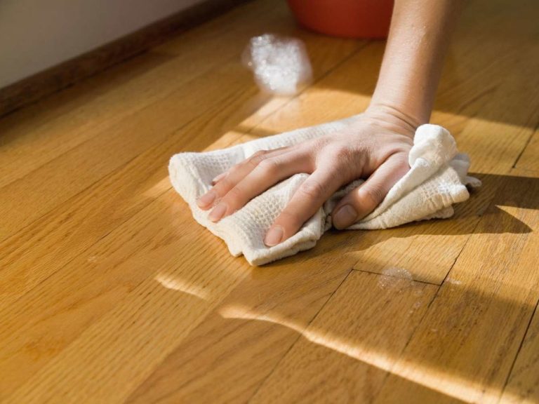 Cleaning unfinished wood floor by hand with a soft cloth during gentle surface care and maintenance