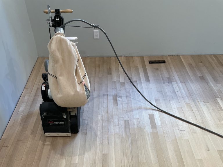 Hardwood floor sanding machine on thick floorboards showing the kind of surface material that affects refinishing potential and long-term durability