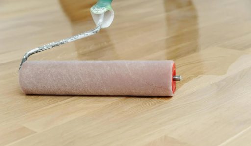 Applying finish to hardwood floor with roller to create an even protective topcoat across the surface