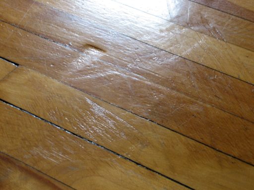 Worn hardwood floor finish before restoration showing scratches dullness and uneven surface wear that no-sand methods may not fully fix