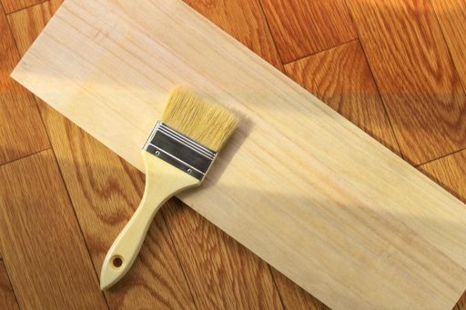 Unfinished wood sample board with brush for testing stain or sealant before floor finishing