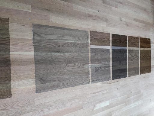 Testing stain colors on hardwood floor to compare tone depth and grain appearance before application