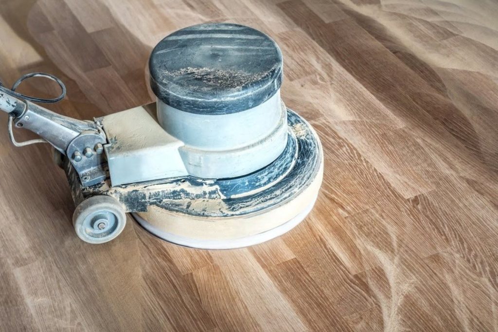 A floor buffer machine is preparing a hardwood floor surface during the refinishing process.