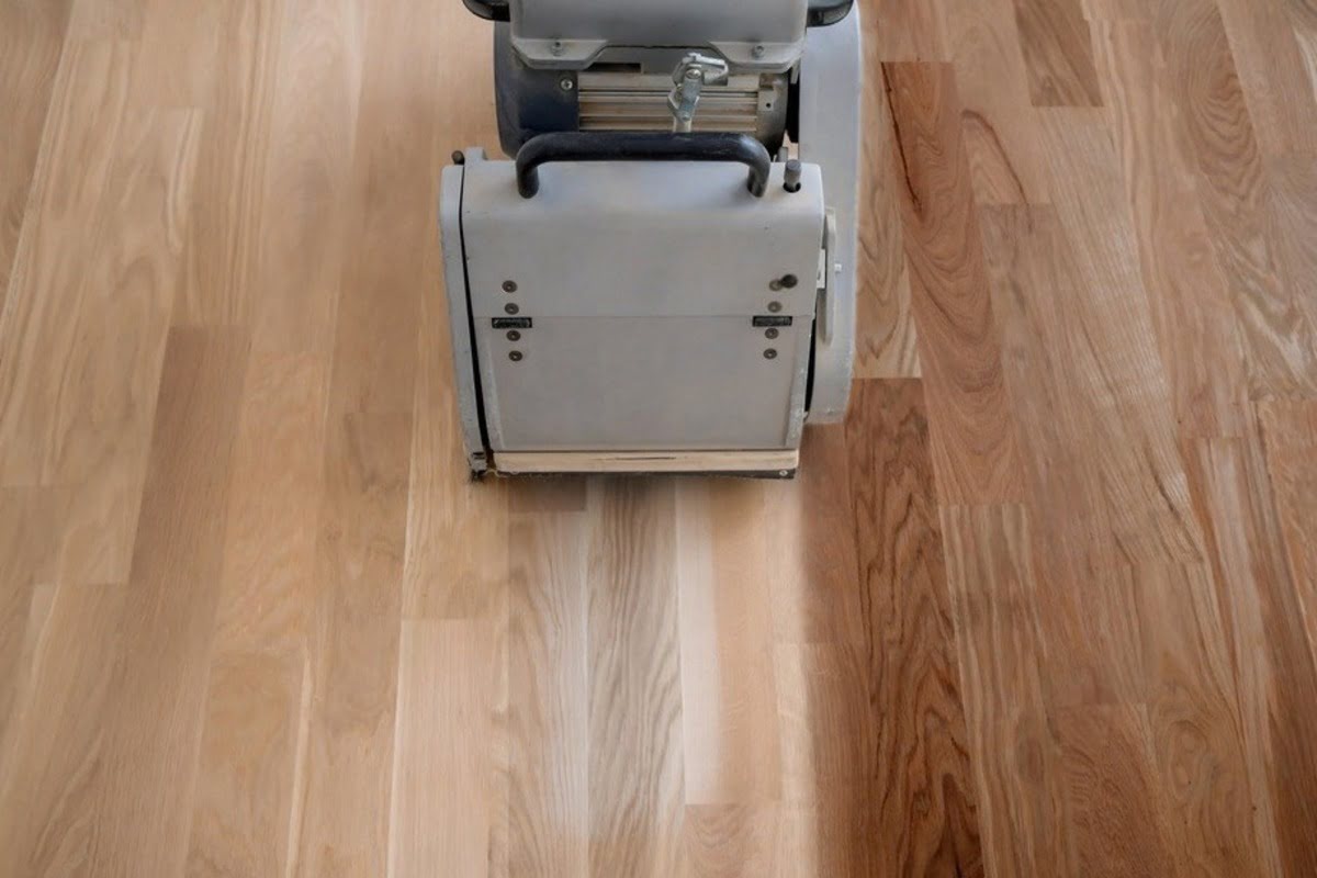 A floor sanding machine is smoothing a hardwood floor during the refinishing process to prepare the surface for a new finish.