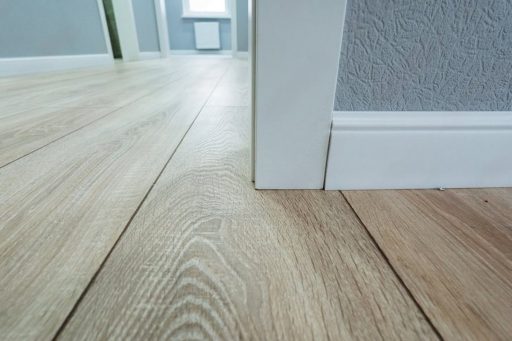 Close-up of hardwood floor boards near baseboard showing gaps and surface condition assessed before sanding and refinishing