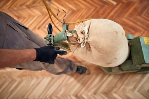 A flooring technician is using a buffing machine on a hardwood floor during the refinishing process.