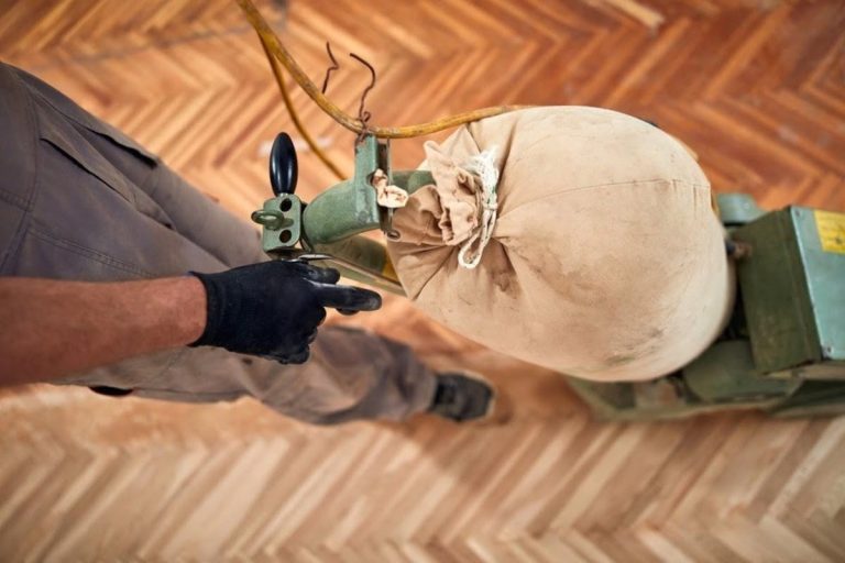 A flooring technician is using a buffing machine on a hardwood floor during the refinishing process.