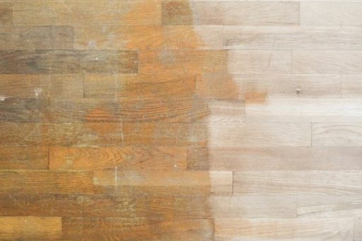 A hardwood floor shows the contrast between the original finish and the freshly sanded wood surface during the refinishing process.